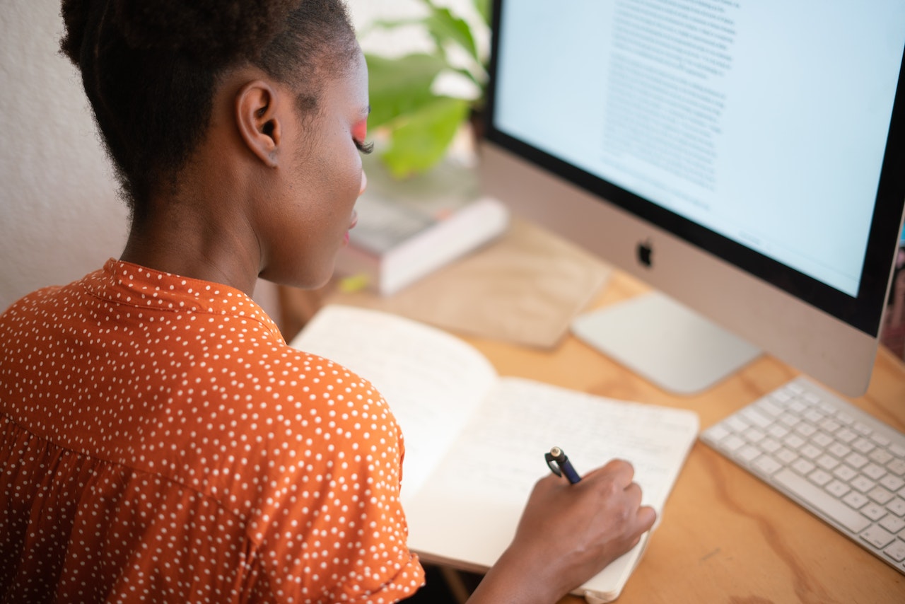 women at computer desk writing in notebook