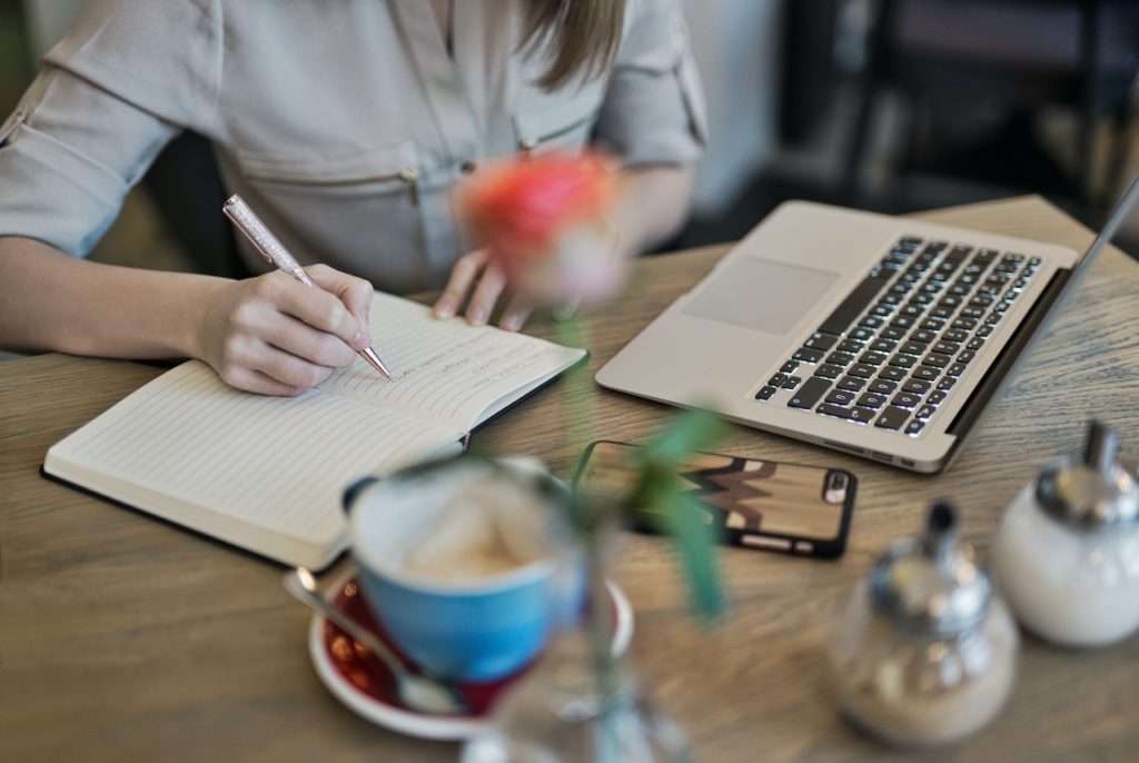 women writing in notebook next to laptop